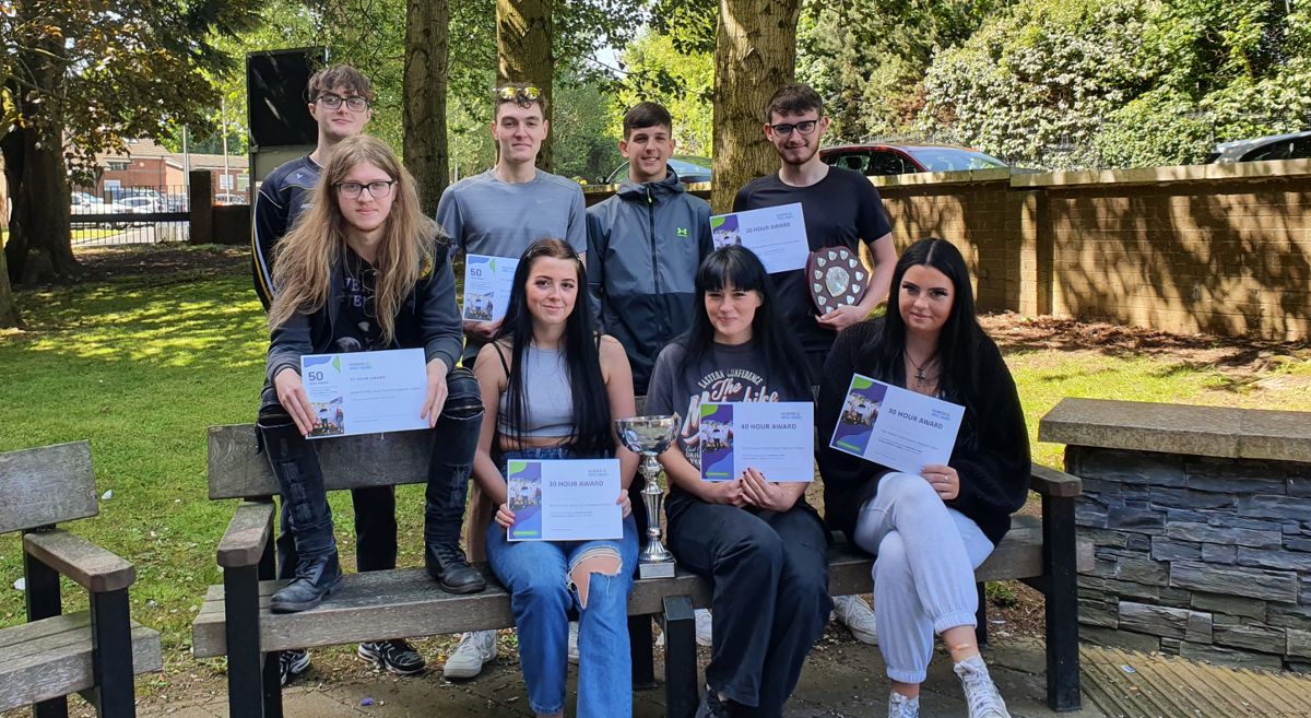 Seated and standing public services students holding certificates outside the Bangor campus.